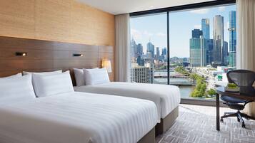 A hotel room with two beds, a desk, and a large window offering a city view.