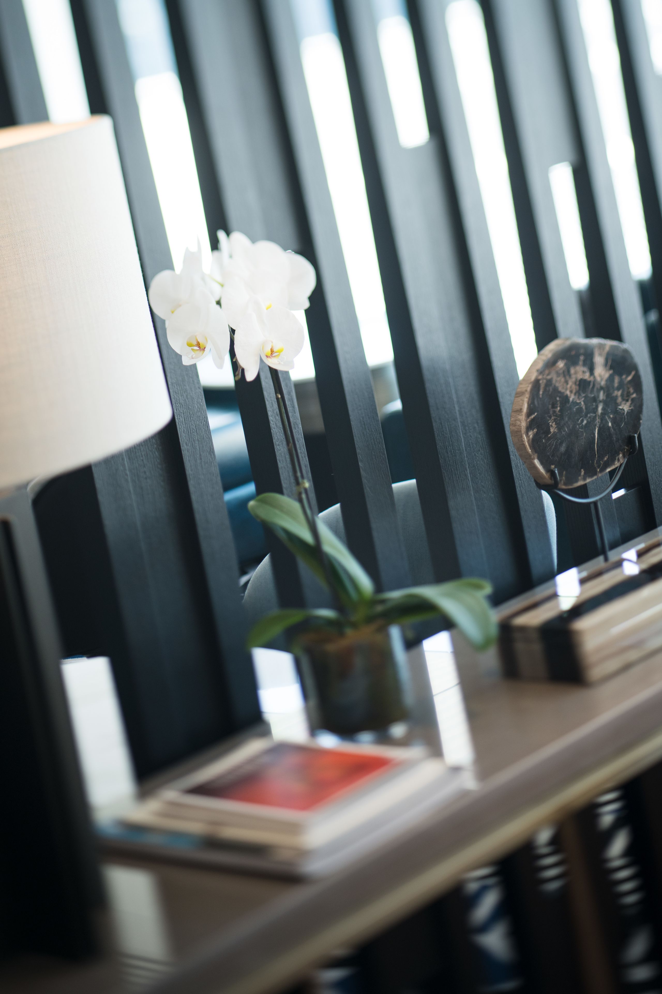 A wooden chair with vertical slats, a white orchid in a pot, a round mirror, and a book on the seat.