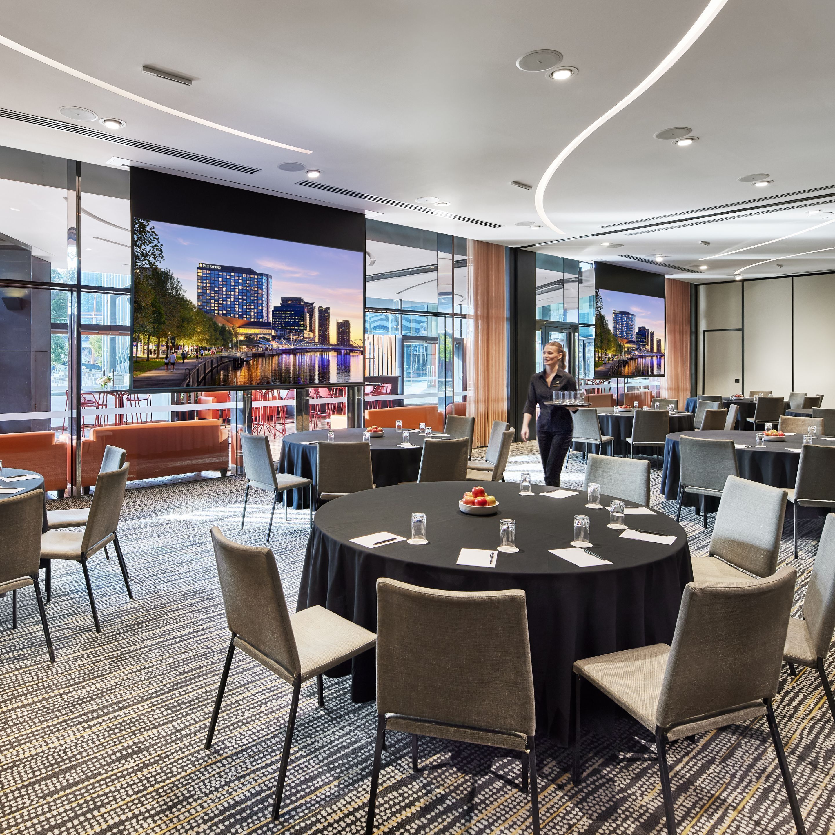 A conference room with round tables, chairs, and a large window with a cityscape view.