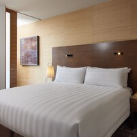 Habitación de hotel con una cama grande, cabecero de madera, mesita de noche, lámpara y un cuadro en la pared.