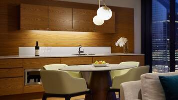 A modern kitchen with wooden cabinets, a central island with chairs, a dining table, and a city view through large windows.