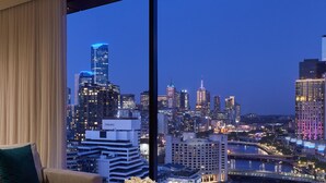 A modern hotel room with a large window offering a city skyline view at dusk. - Pan Pacific Melbourne (South Wharf)