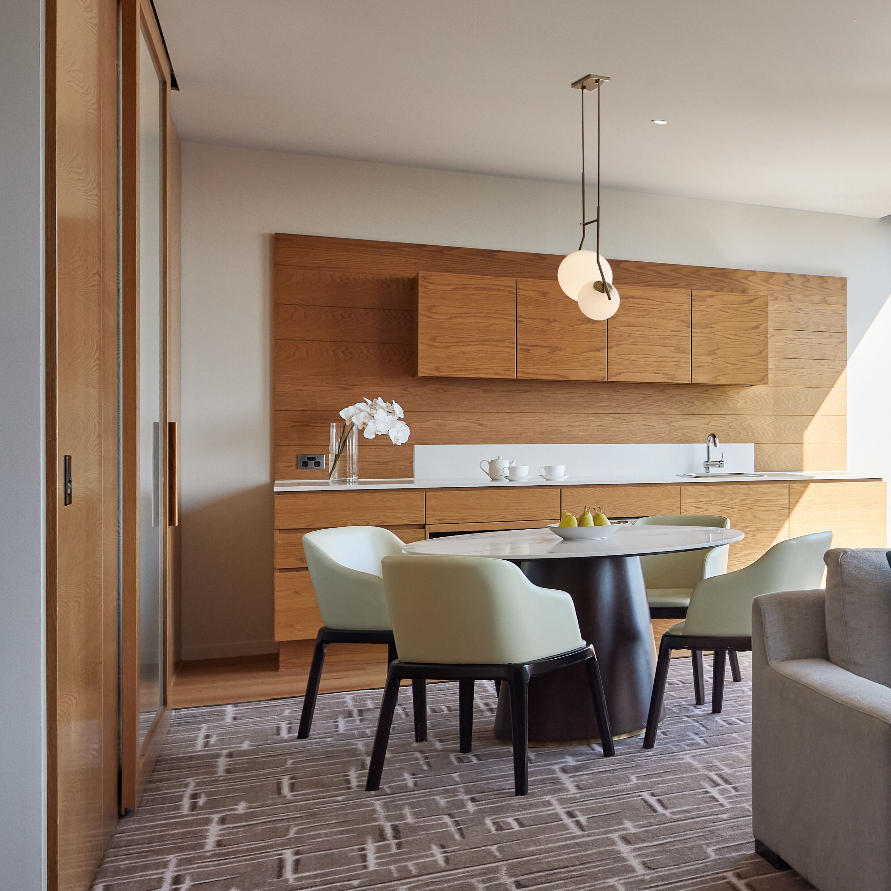 Een moderne keuken met houten kasten, een eettafel met stoelen en een hangende lamp.