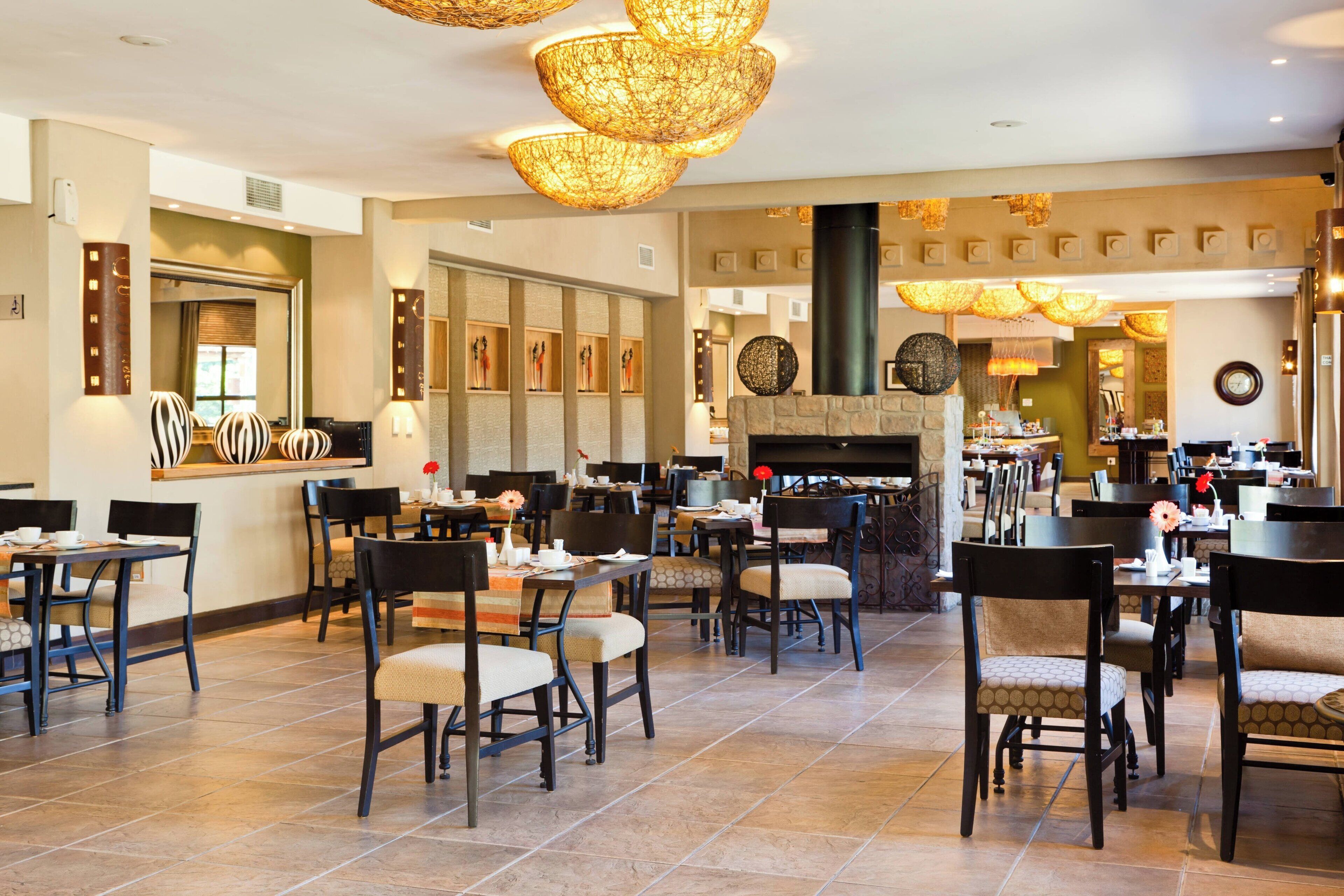 A spacious hotel lobby with multiple dining areas, a fireplace, and modern lighting fixtures.