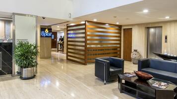 Eine geräumige Lobby mit modernem Design, inklusive einer Rezeption, einer Sitzecke und einer Treppe zu einer oberen Ebene.