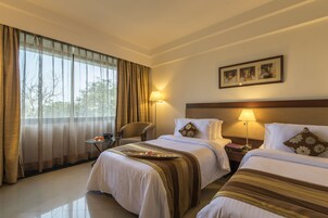 Una habitación de hotel con dos camas, una silla, una mesita y una lámpara.
