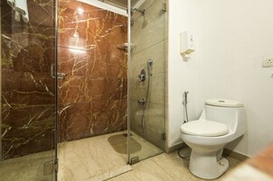 Un baño con ducha envuelta en vidrio, inodoro y suelo de mármol.