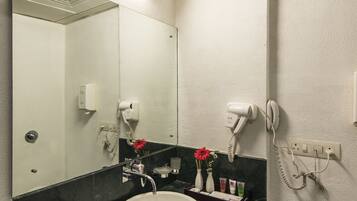 A bathroom with a white sink, dark countertop, and a mirror. There are hair dryers and a phone on the wall.