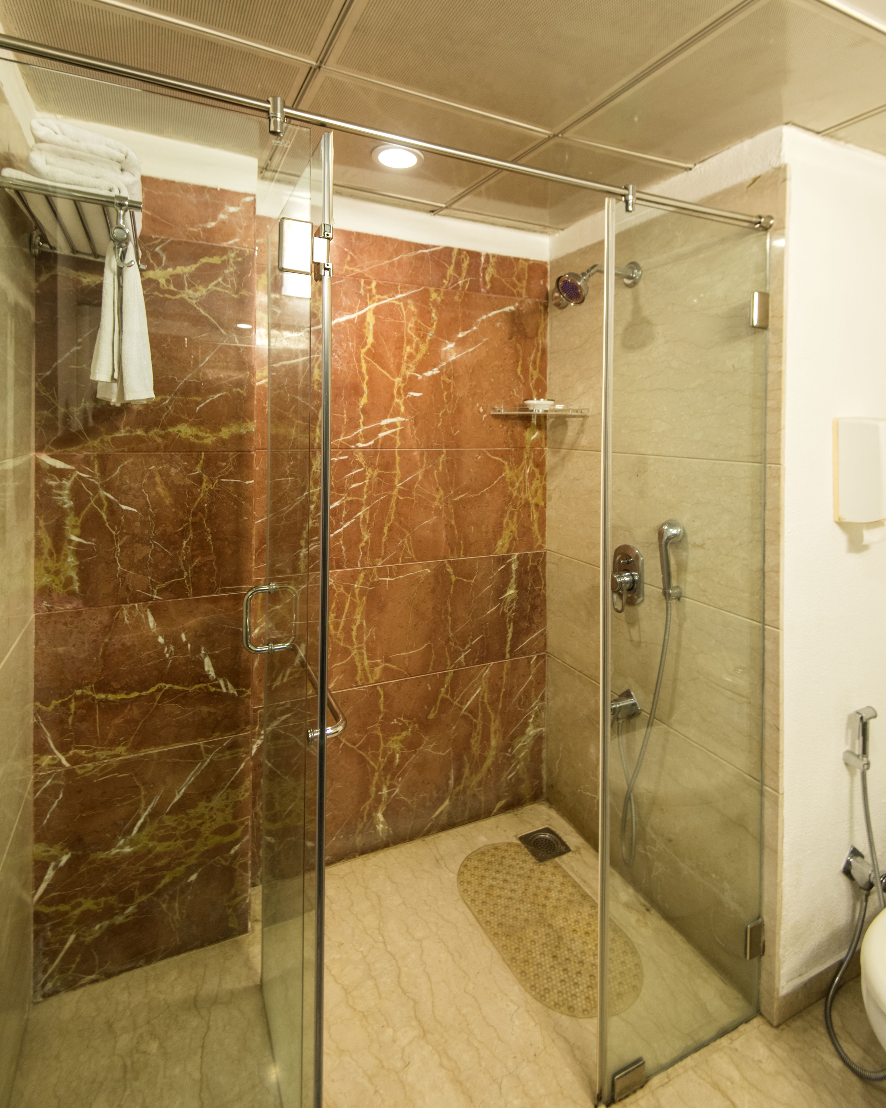 Un baño moderno con cabina de ducha de vidrio, paredes de mármol e inodoro empotrado.