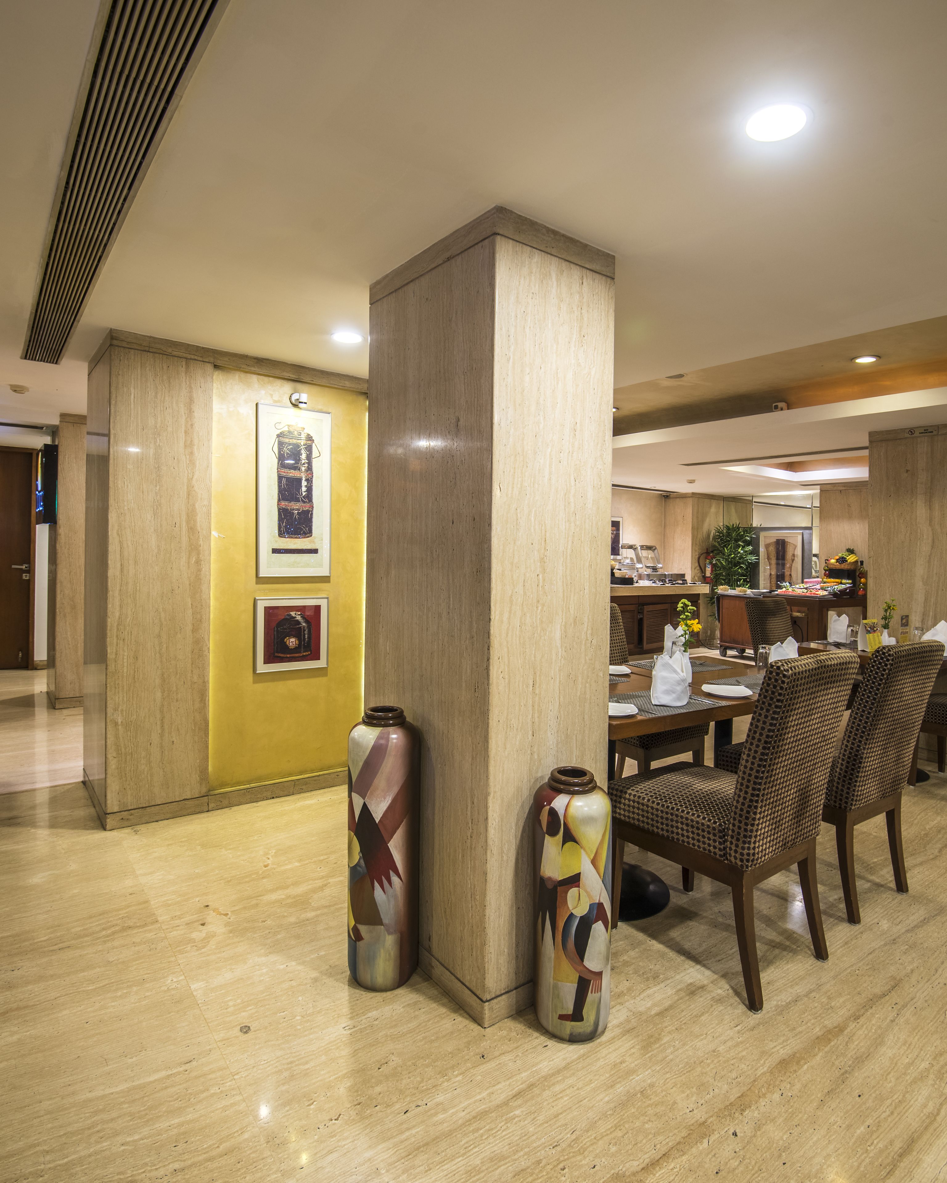 A hotel dining area with a wooden table, chairs, and two decorative vases.