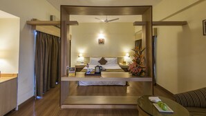 A hotel room with a bed, bedside tables, a ceiling fan, a nightstand, a coffee maker, a tray with snacks, and a flower arrangement. - Phoenix Hotel (Pune)