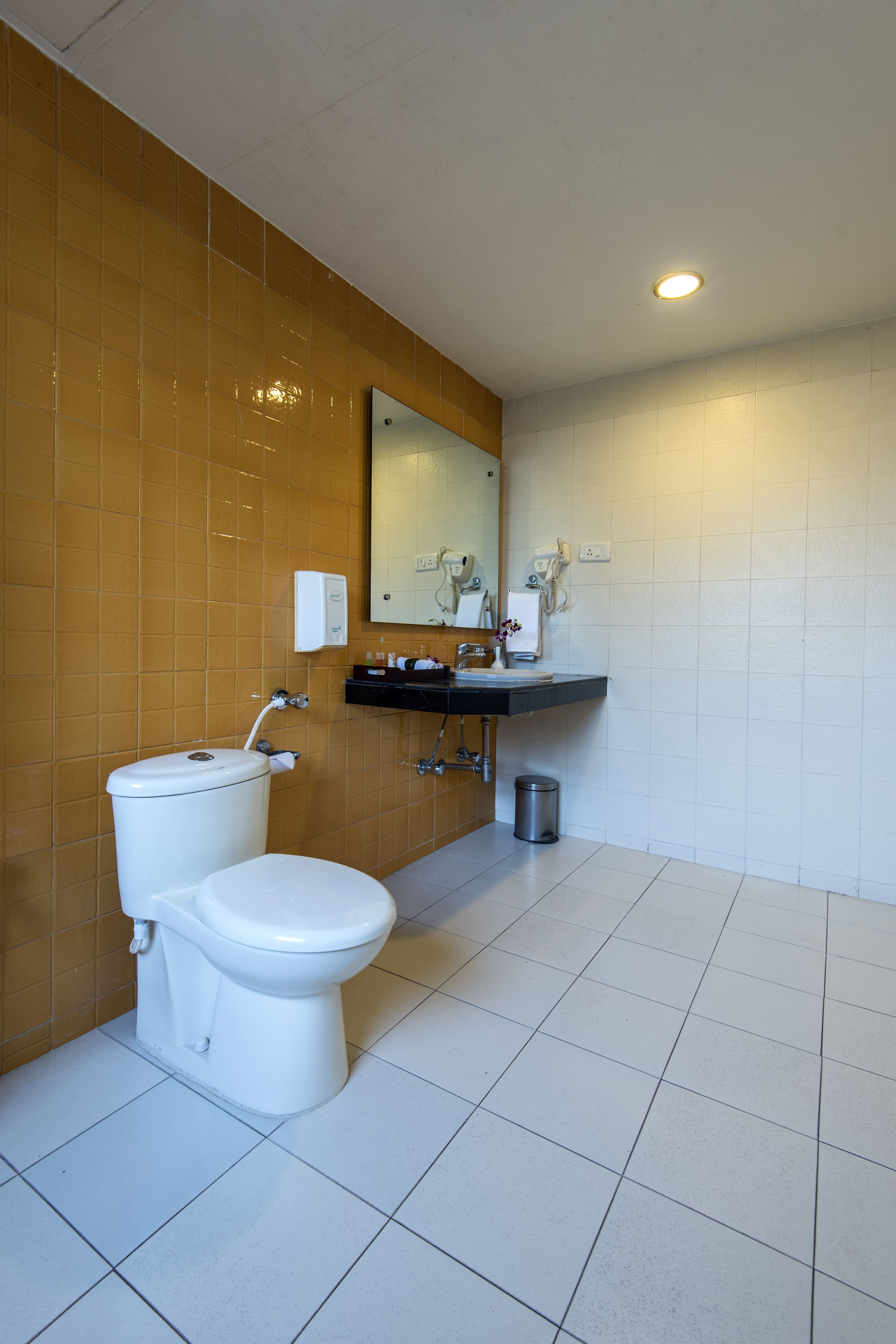 Un baño con inodoro, lavamanos, espejo y paredes de azulejos.
