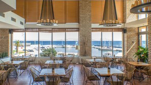 Um restaurante com grandes janelas de frente para uma marina e o mar.