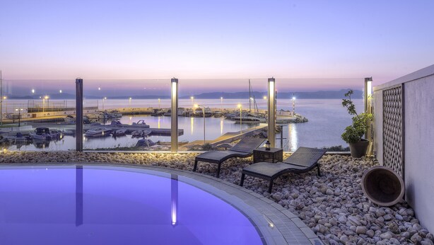 Piscina com espreguiçadeiras e vista para um porto ao anoitecer.