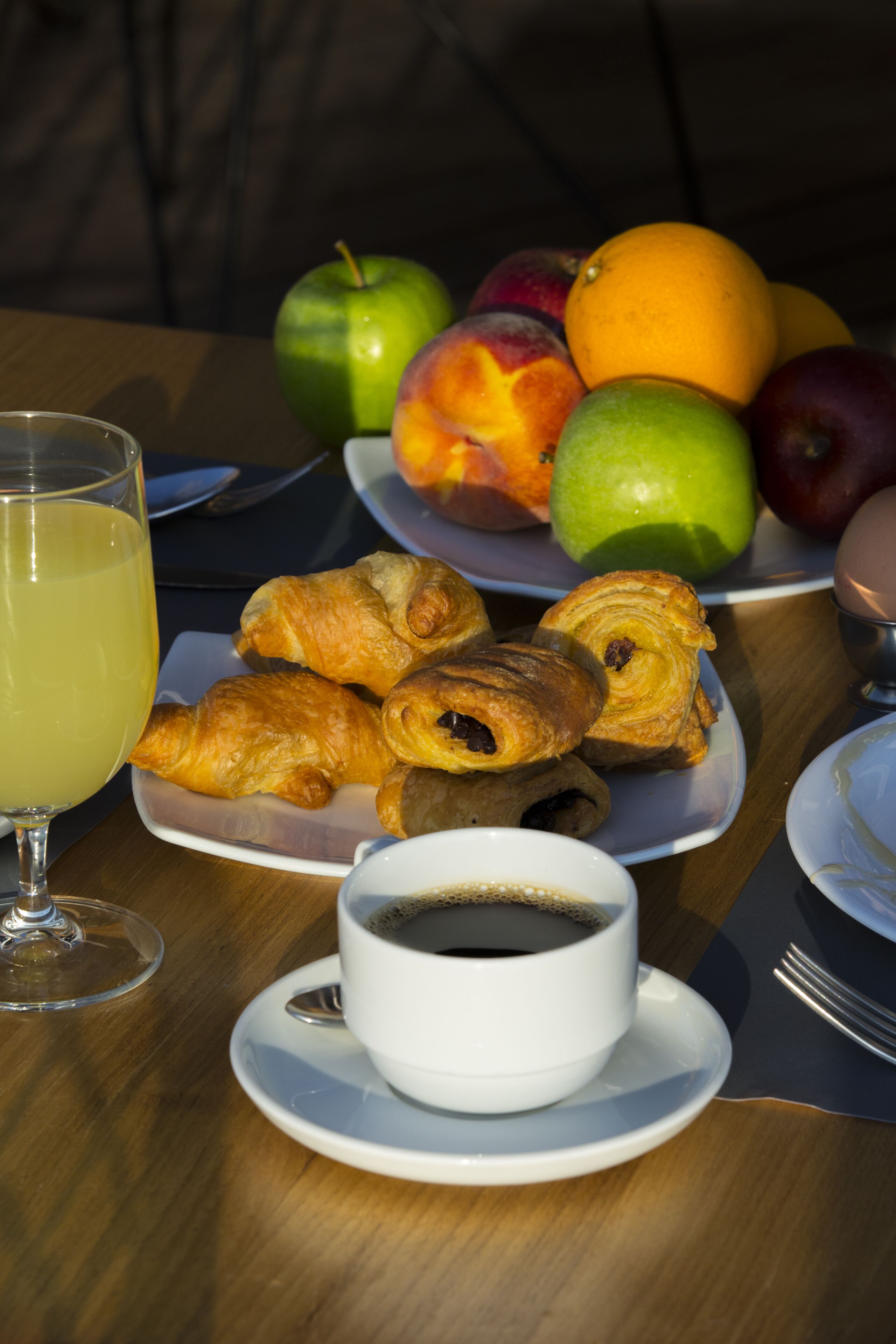Une table de petit-déjeuner avec des croissants, du café et des fruits.
