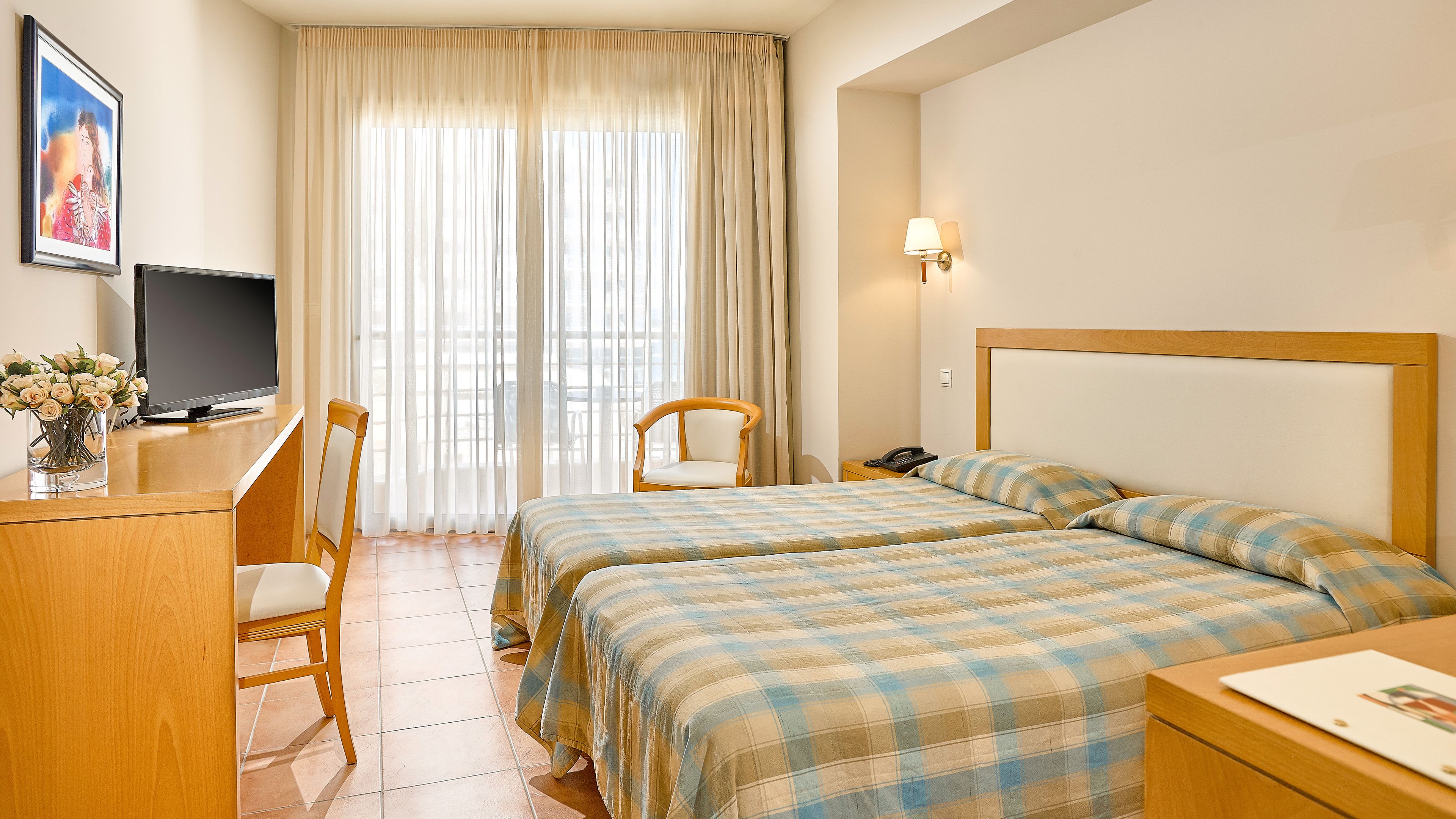 Habitación de hotel con dos camas, un escritorio, una silla, un televisor y un cuadro en la pared.