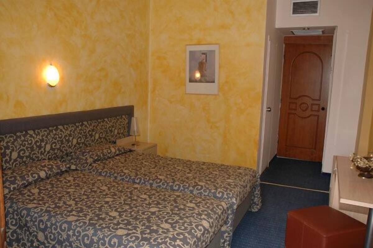 Un dormitorio con colcha estampada, lámpara de noche, cuadro enmarcado en la pared y puerta de madera.