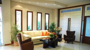 Ein Wohnzimmer mit einer Couch, zwei Sesseln, einem Couchtisch und einem großen Fenster mit Blick auf Grünflächen.