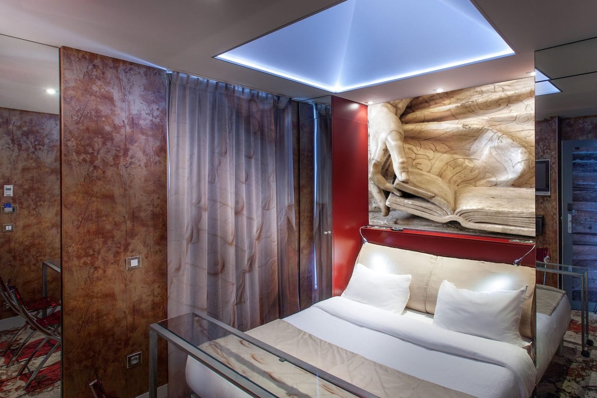 Una habitación de hotel moderna con una cama de cristal, un tragaluz, una pared de mármol y una pared de acento roja.