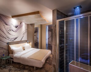 A modern hotel room with a large bed, a shower with a glass door, and a decorative wall mural. - Apostrophe Hotel (Paris)