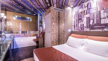 Ein modernes Hotelzimmer mit einem großen Bett, einem Badezimmer mit Glasdusche und einer Wand mit abstrakter Kunst.