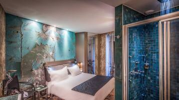 Ein Hotelzimmer mit einem großen Bett, einer Dusche mit blauen Kacheln und einer Steinwand mit abblätternder Farbe.