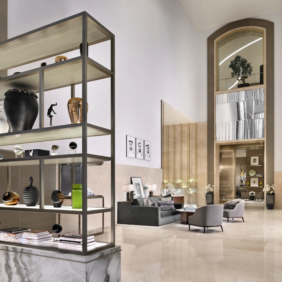 A modern interior with a marble reception desk, a multi-tiered display shelf, a cozy seating area, and a large arched mirror.
