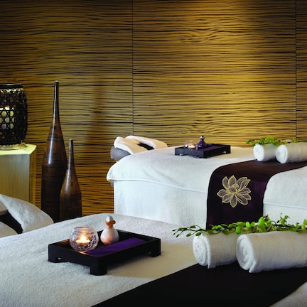 A spa room with two beds, a wooden wall, a small table with a candle, and towels.