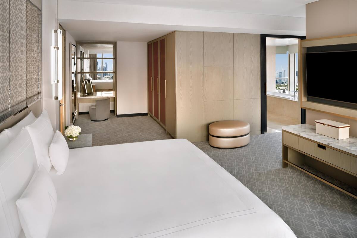 A modern hotel room with a large bed, a TV, a desk, and a wardrobe.