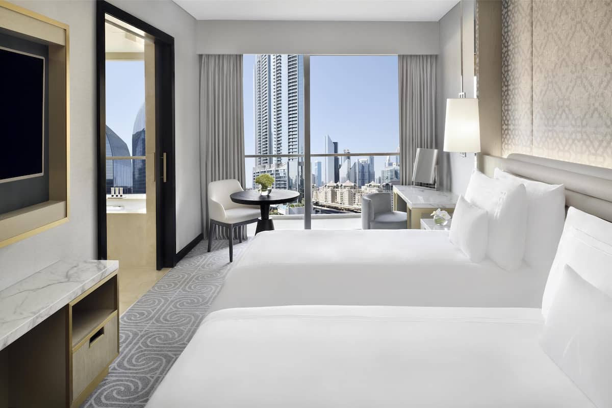 A hotel room with a large bed, a desk with a chair, a TV, and a view of the cityscape.