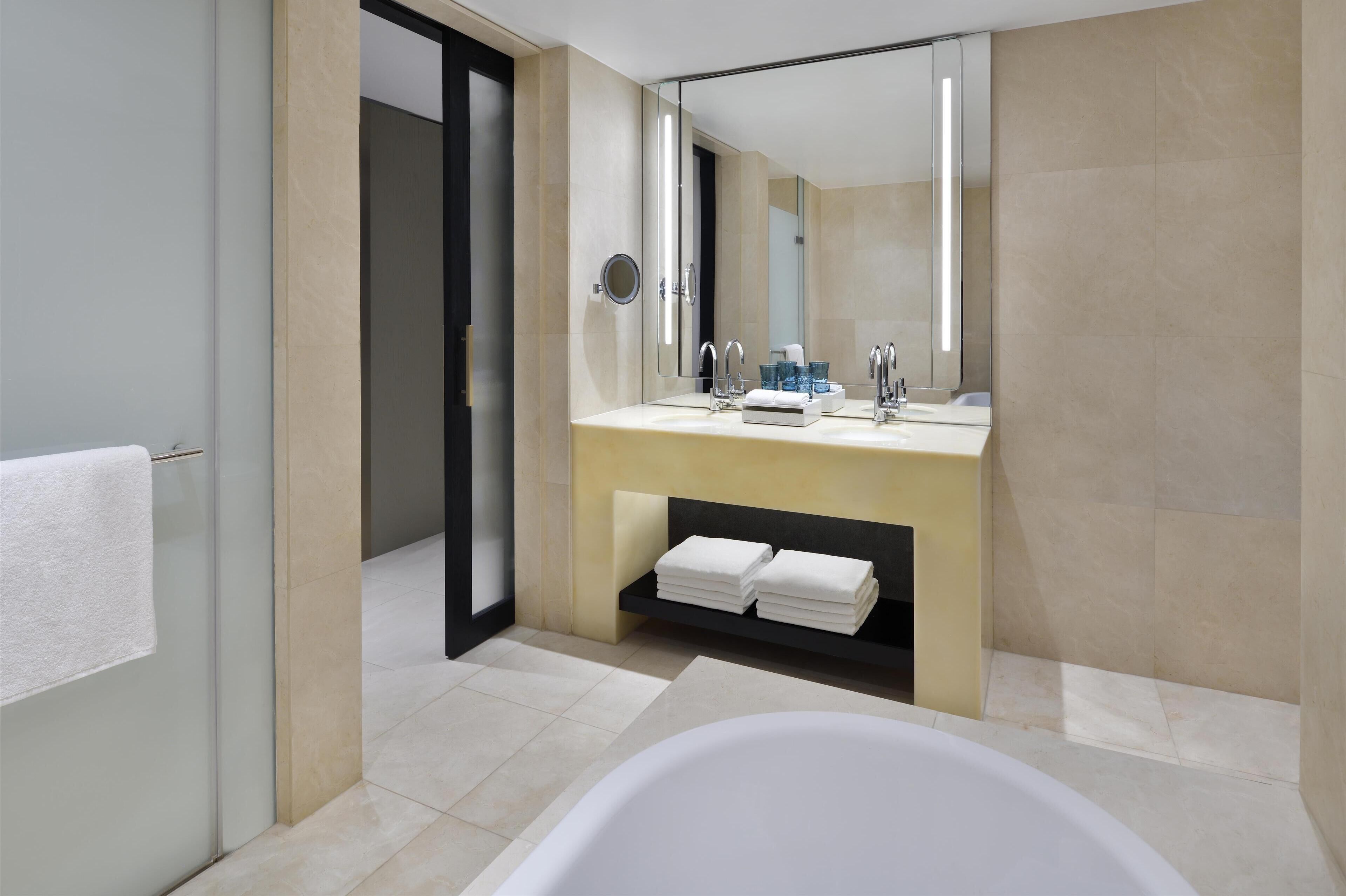 Un baño moderno con un espejo grande, dos lavamanos, una bañera y un perchero para toallas.
