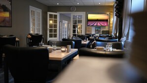 A restaurant with booths and tables, a clock on the wall, and a TV screen displaying a sunset. - Prinsen Hotel (Aalborg)