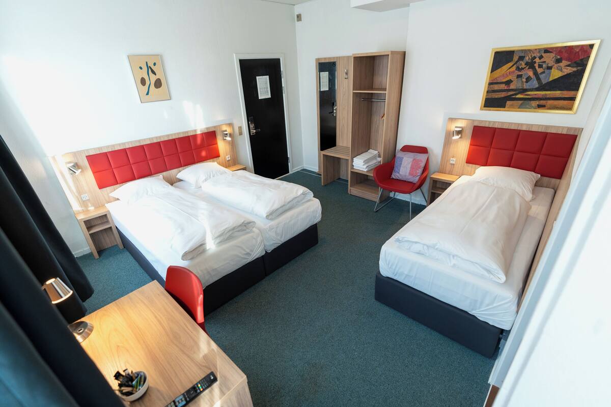 A hotel room with two beds, a desk, a chair, a wardrobe, and artwork on the walls.