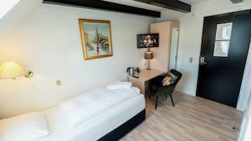 Una habitación con cama, escritorio, silla, un cuadro, televisor y puerta con marco negro.