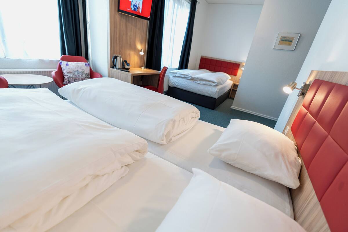 A hotel room with two beds, a desk, a chair, and a TV on the wall.