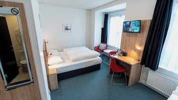 Habitación de hotel con cama, escritorio, silla, televisor y ventana con cortinas.