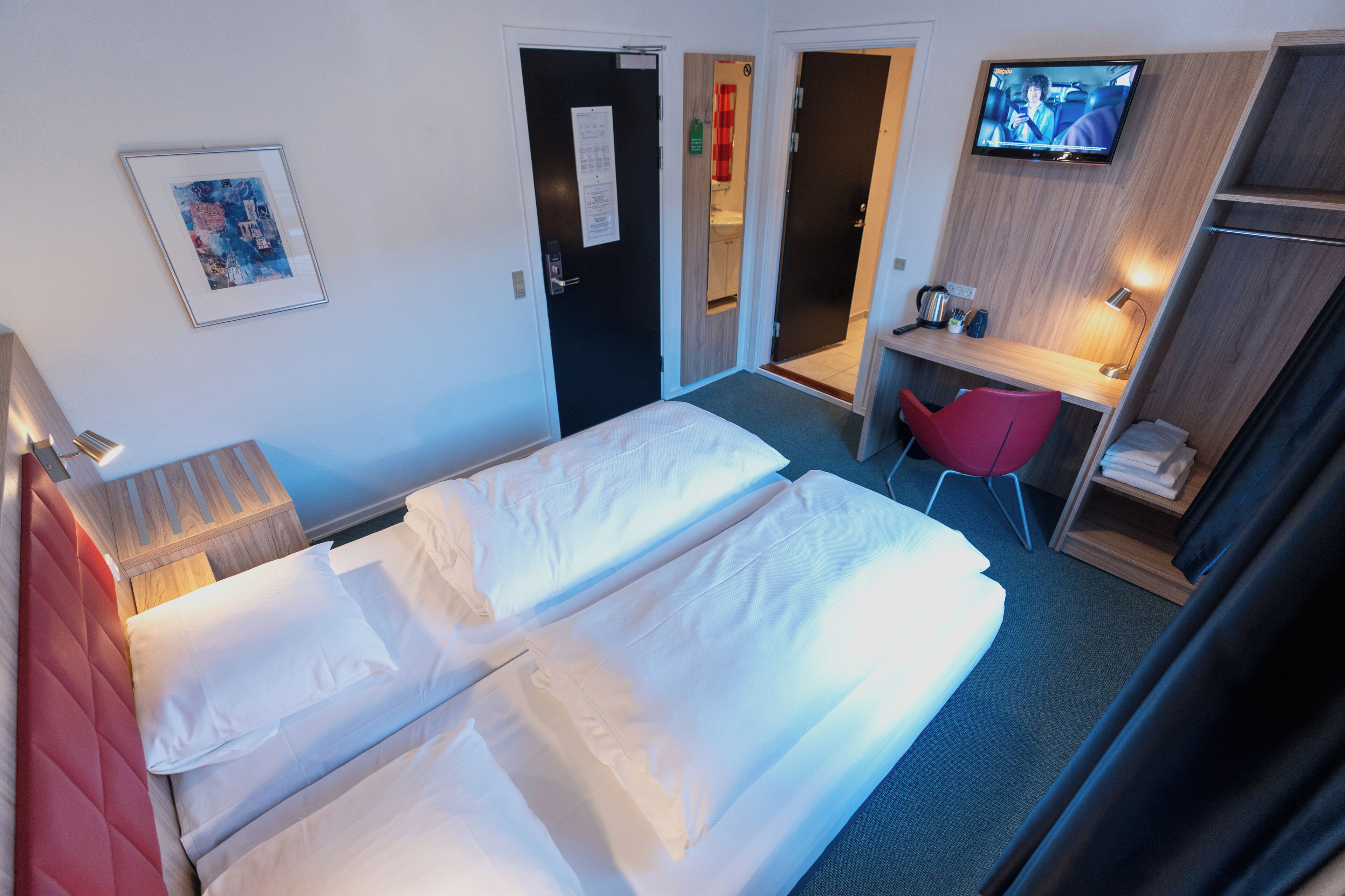 A hotel room with two beds, a desk, a TV, and a red chair.