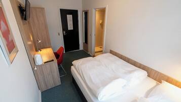 Habitación de hotel con cama, escritorio con lámpara, una silla roja y zona de ducha.