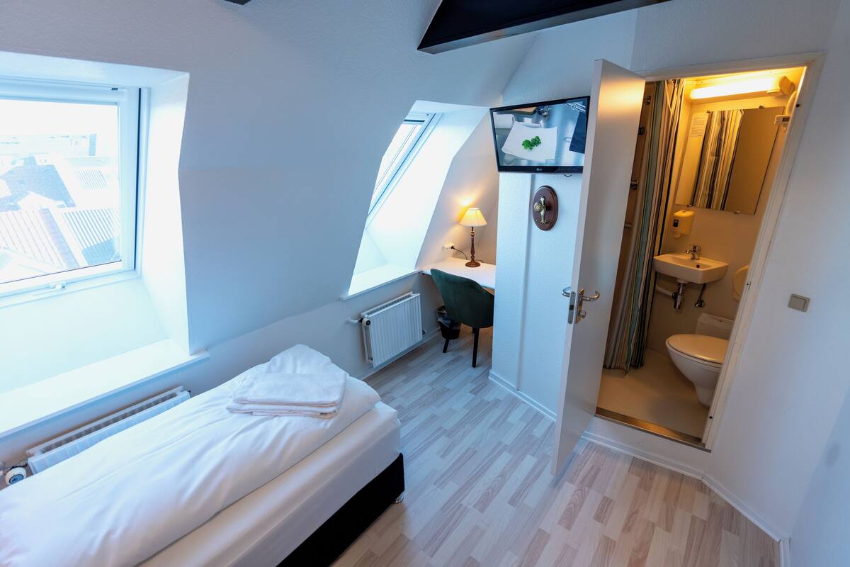 A bedroom with a bed, a desk, and a bathroom.