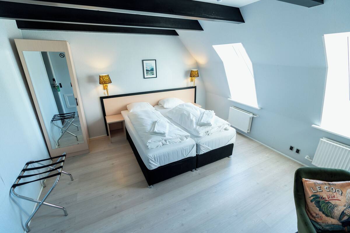 A bedroom with a bed, a mirror, two wall-mounted lamps, a radiator, and a window.
