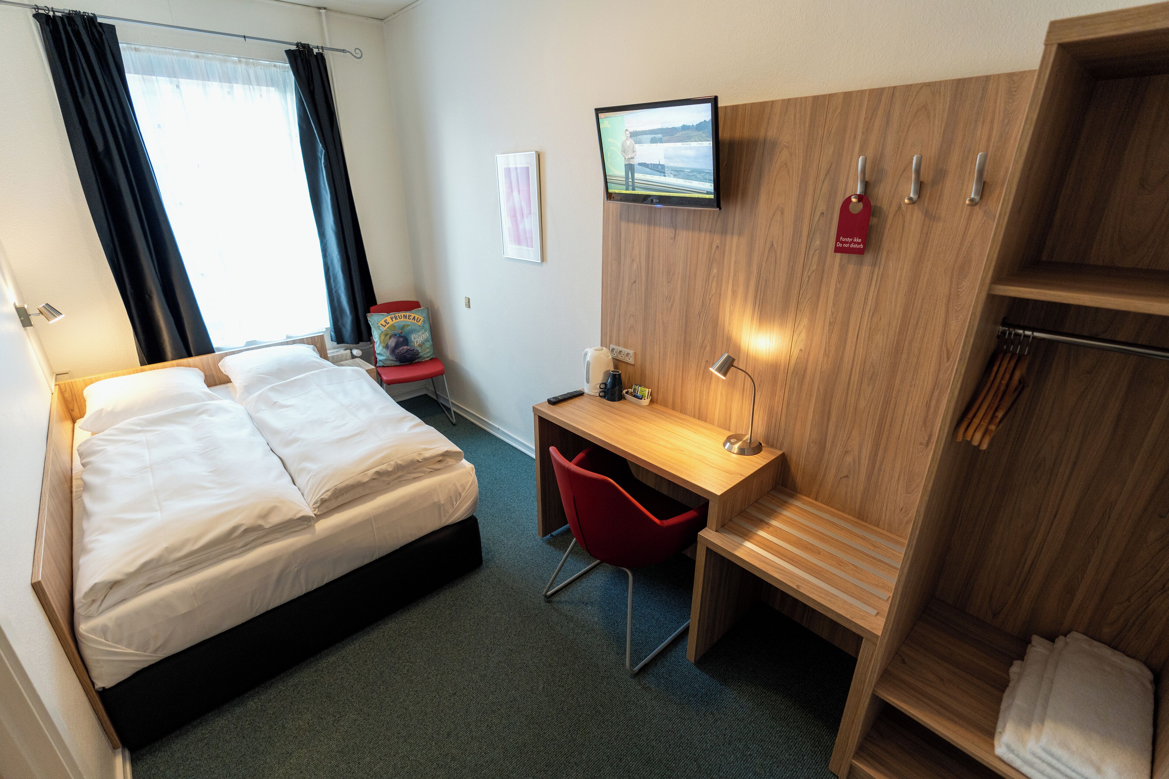 A hotel room with a bed, a desk, a chair, a TV, and a wardrobe.