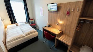 A hotel room with a bed, a desk, a chair, a TV, and a wardrobe.