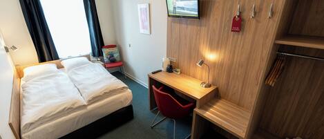 A hotel room with a bed, a desk, a chair, a TV, and a wardrobe.