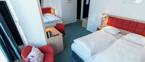 A hotel room with a large bed, a desk with a chair, a television, and a red upholstered headboard.