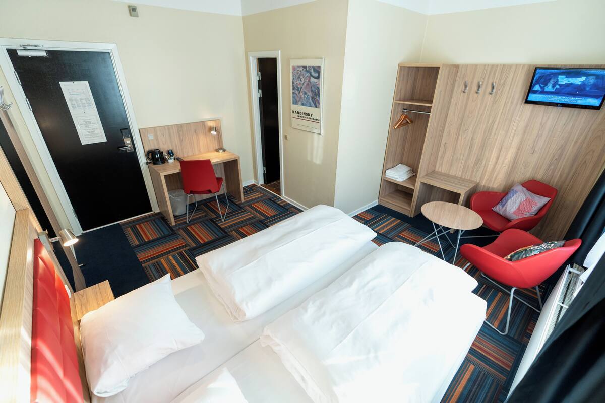 A hotel room with a bed, a desk, a chair, a TV, and a wardrobe.