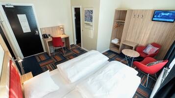 A hotel room with a bed, a desk, a chair, a TV, and a wardrobe.