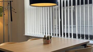 Un comedor moderno con una mesa de madera, sillas negras y beige, una lámpara colgante negra y un ventanal con persianas verticales.