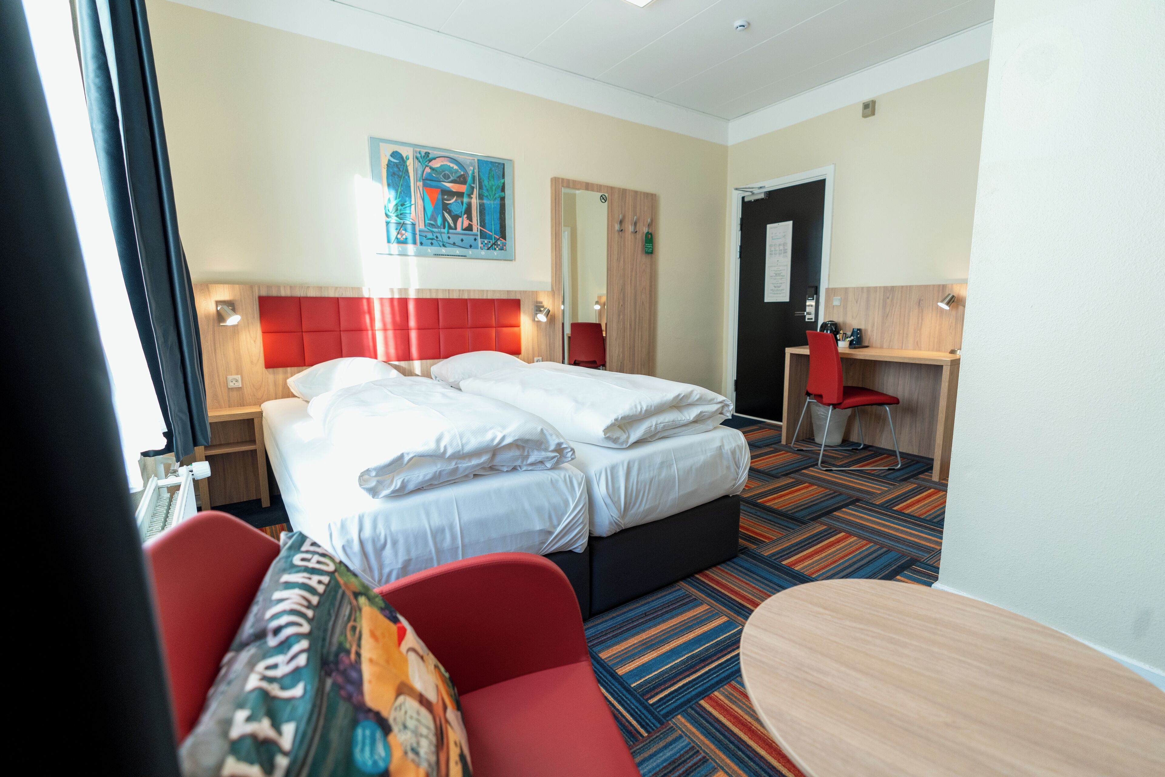 A hotel room with two beds, a desk, a chair, and a colorful carpet.