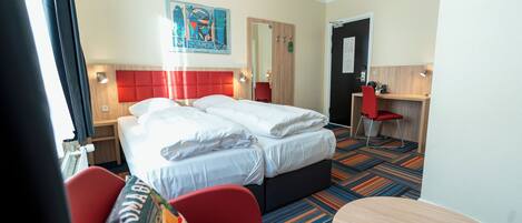 A hotel room with two beds, a desk, a chair, and a colorful carpet.