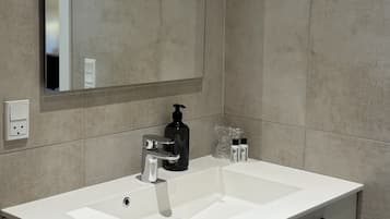 Ein Badezimmer mit einem weißen Waschbecken, einem Spiegel, einem schwarzen Seifenspender und zwei Duschgelflaschen.